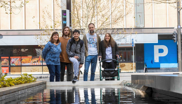 Five people are standing in front of a pond and smiling at the camera.