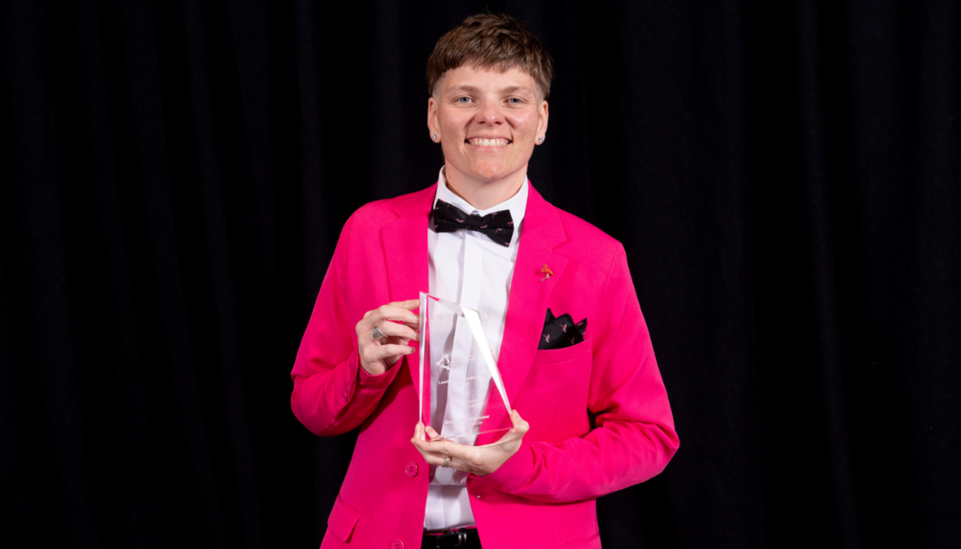 City of Adelaide team member Steph stands holding a trophy. She wears a bright pink suit and smiles to the camera.