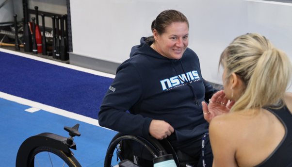 Louise Sauvage is smiling at work, while coaching a person with their back to the camera.
