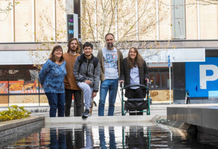 Five people are standing in front of a pond and smiling at the camera.