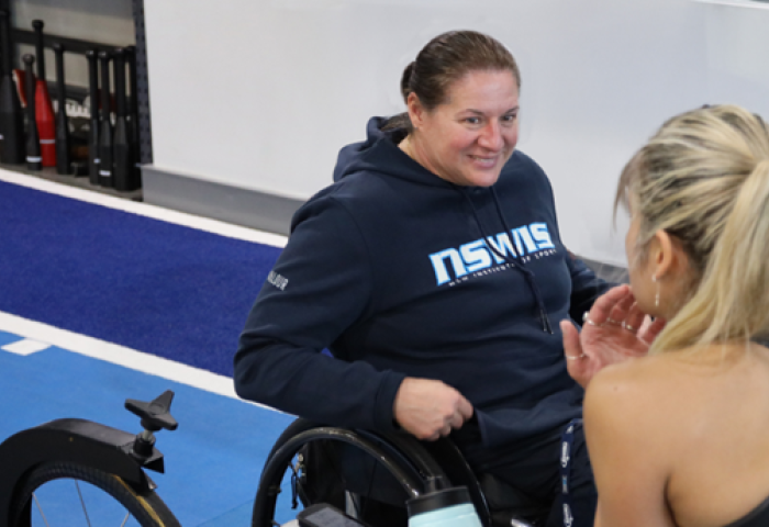 Louise Sauvage is smiling at work, while coaching a person with their back to the camera.