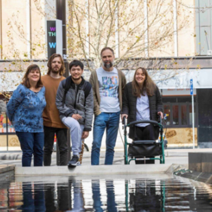 Five people are standing in front of a pond and smiling at the camera.