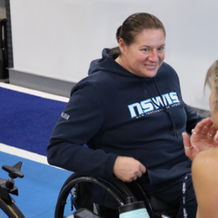 Louise Sauvage is smiling at work, while coaching a person with their back to the camera.